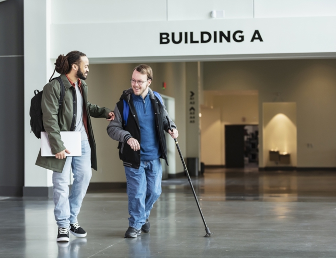 Person walking with a disabled student in school hallway.