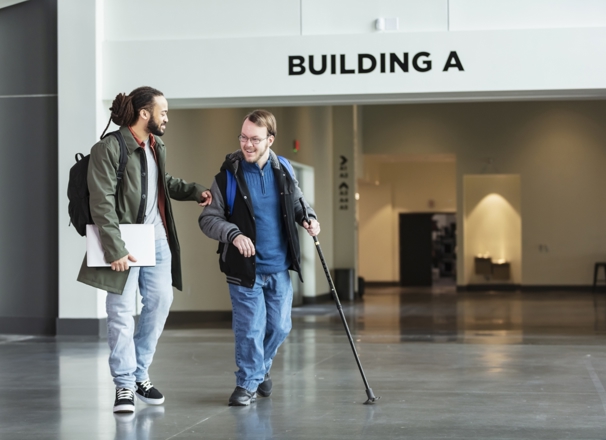 Person walking with a disabled student in school hallway.