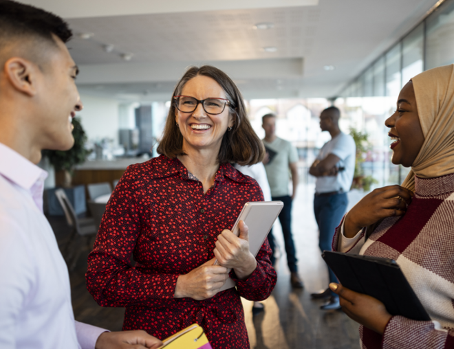 3 people happily talking while standing in office.
