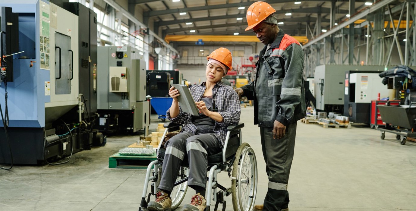 Two employees in a manufacturing shop review information on a tablet.