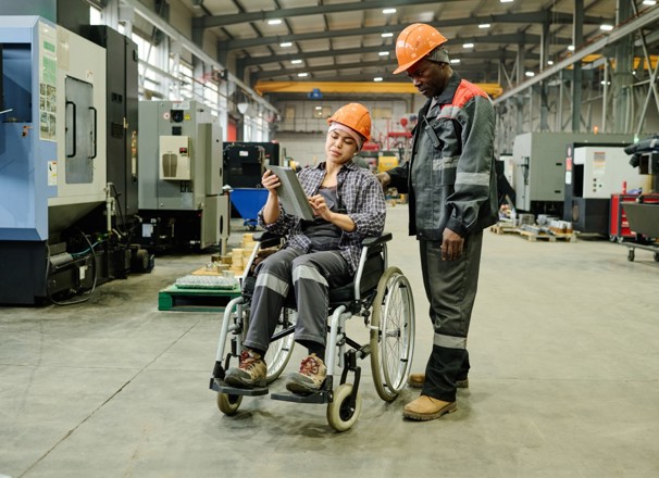 Two employees in a manufacturing shop review information on a tablet.