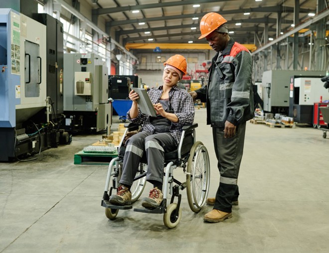 Two employees in a manufacturing shop review information on a tablet.