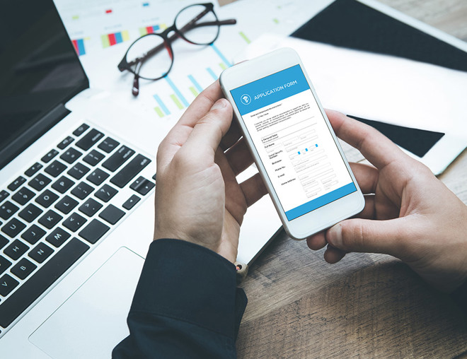 person holding smartphone with application form, laptop, glasses, paperwork
