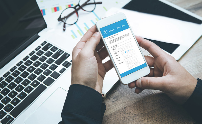person holding smartphone with application form, laptop, glasses, paperwork