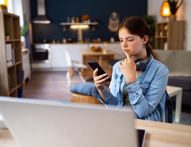 Teenager looking thoughtfully at smartphone.