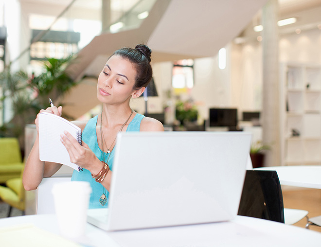 Businesswoman with laptop writing on notepad in office