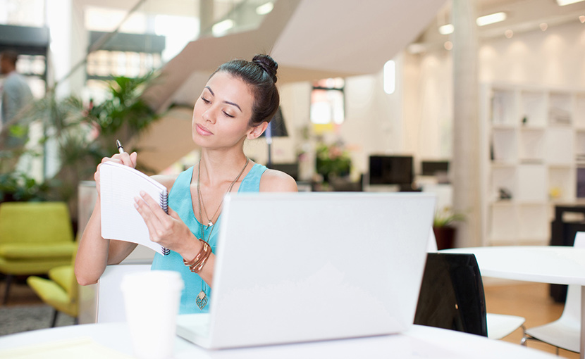 Businesswoman with laptop writing on notepad in office