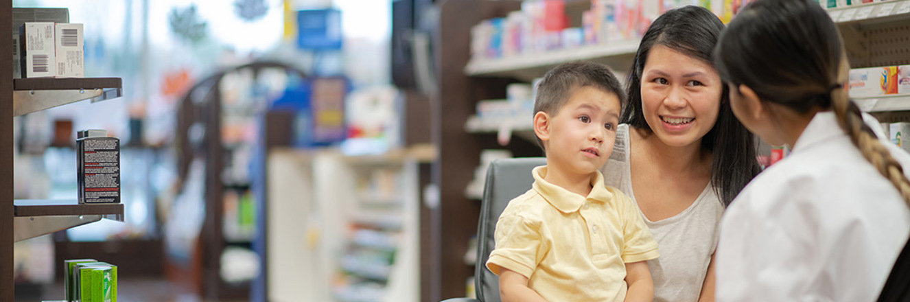 Boy sits on Mothers lap while they talk with the pharmacist