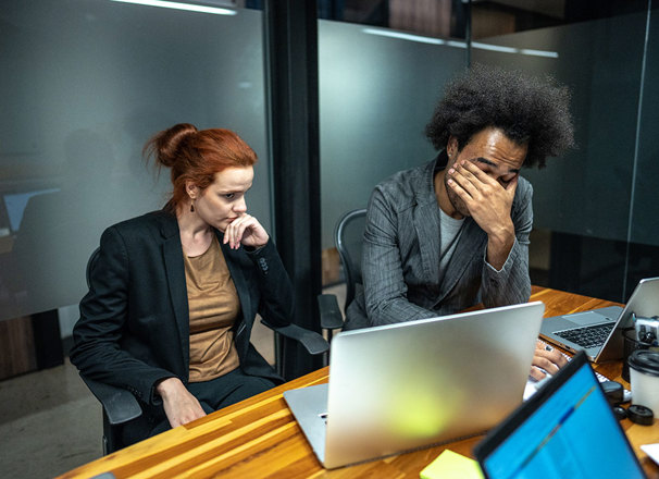 2 colleagues at desk in front of laptop looking frustrated