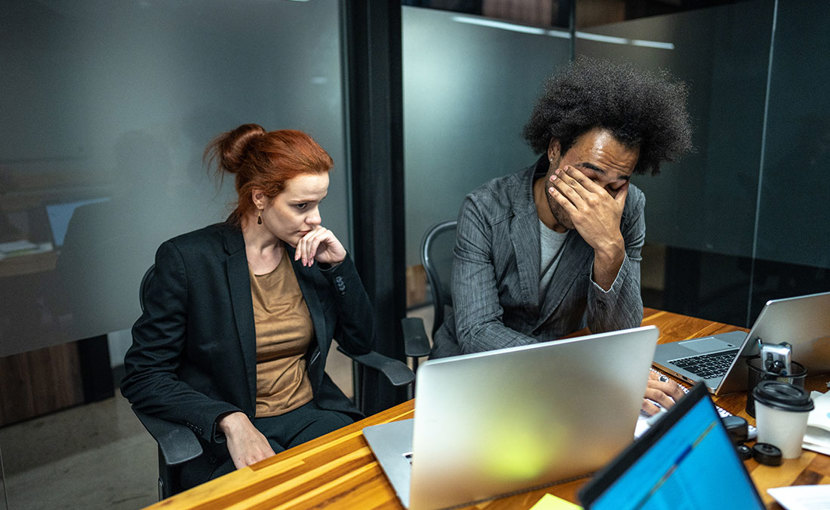 2 colleagues at desk in front of laptop looking frustrated