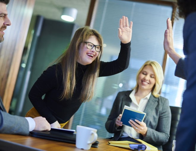 Coworkers high-five each other over a conference room table. 